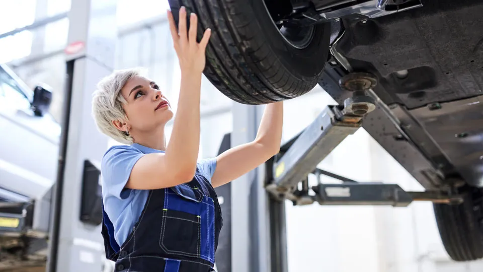 Mechanikerin prüft ein Rad an einem Fahrzeug auf der Hebebühne